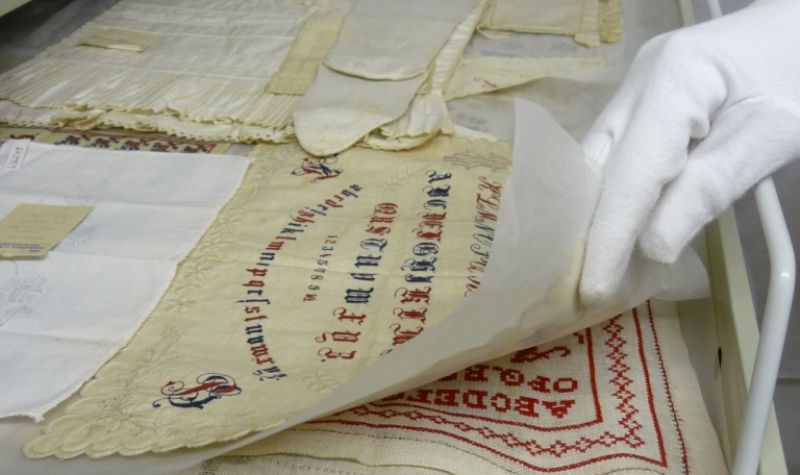 geöffneter Schieber eines Textilschrankes, im Vordergrund liegen Stickmustertücher